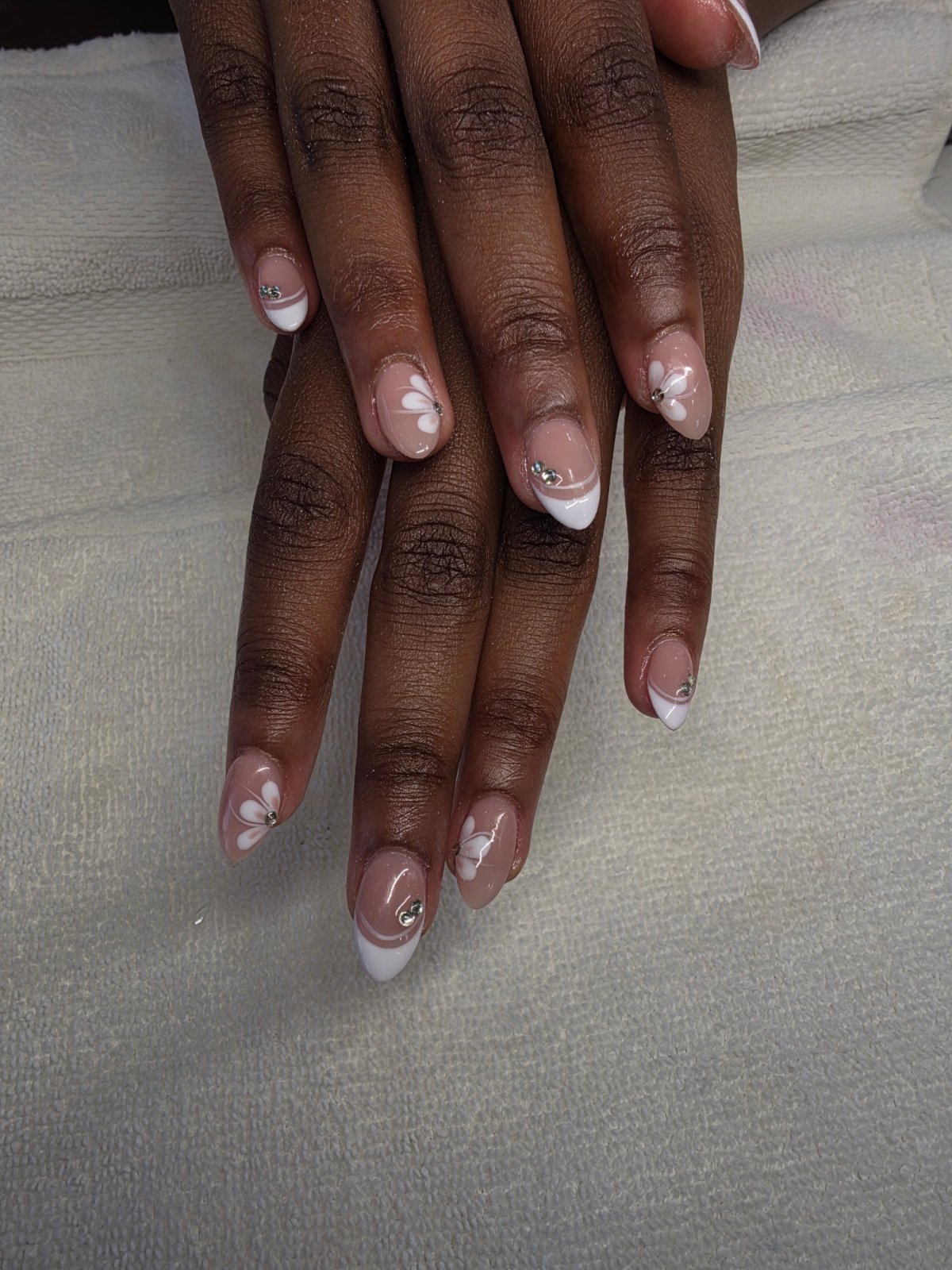 Almond shaped builder gel full set with a sheer nude base, white French tips, hand painted white petal flowers and small rhinestones