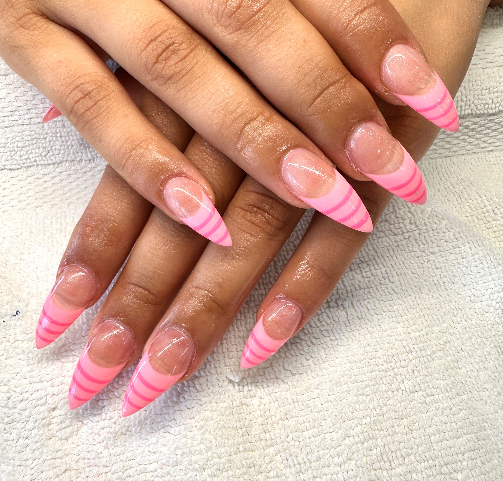 Long stiletto nails with sheer pink base and bubblegum pink French tips striped in a deeper pink, resting on a white salon towel